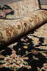 Load image into Gallery viewer, A close-up of a patterned area rug with a rolled section showing the cream and floral design, placed over a black rug with matching floral motifs.