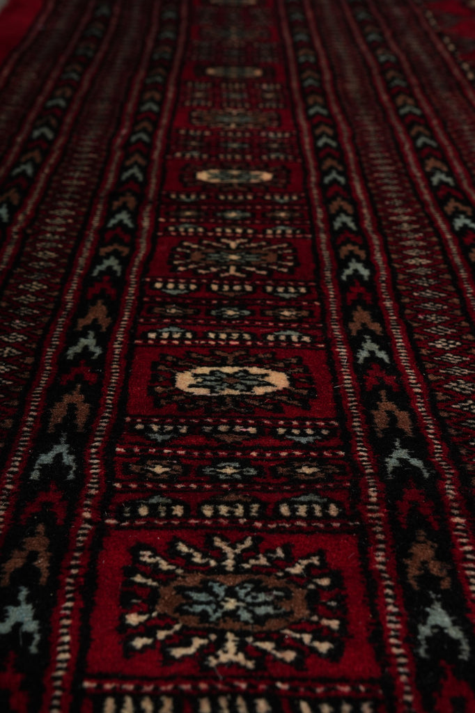 A close-up view of a traditional patterned rug with deep red fields, black geometric borders, and cream and beige central medallions.