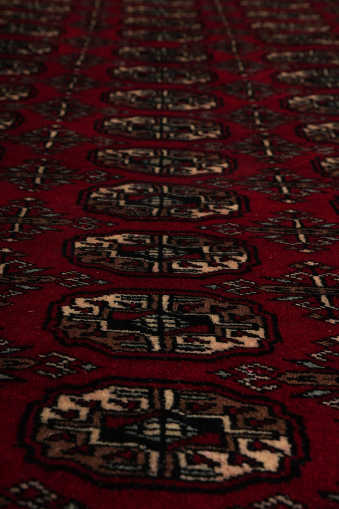 A close-up of a red patterned rug with repeating geometric medallion motifs in beige, black, and brown.