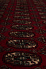 Load image into Gallery viewer, A close-up of a red patterned rug with repeating geometric medallion motifs in beige, black, and brown.