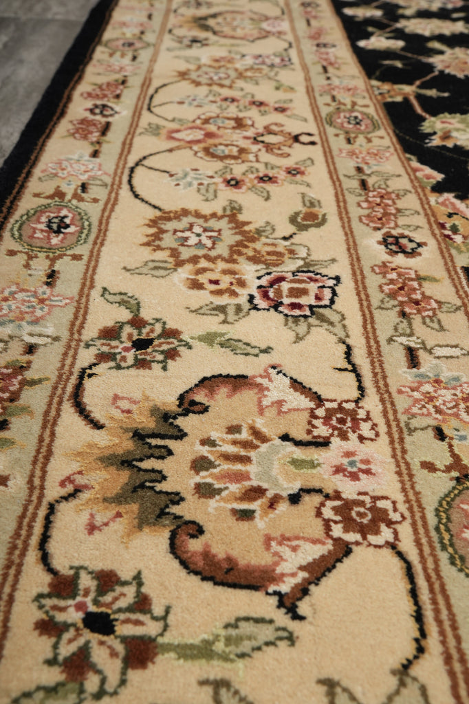 A close-up view of a traditional patterned area rug runner with floral motifs in beige, brown, pink, and green on a cream background.