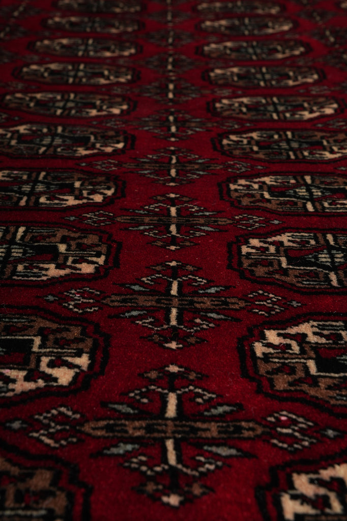 A close-up of a red patterned rug with repeating geometric and floral motifs in beige, black, and brown.