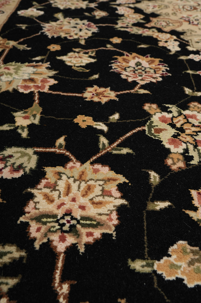 Close-up of a traditional floral area rug with a black background and cream, beige, and muted pink floral motifs.