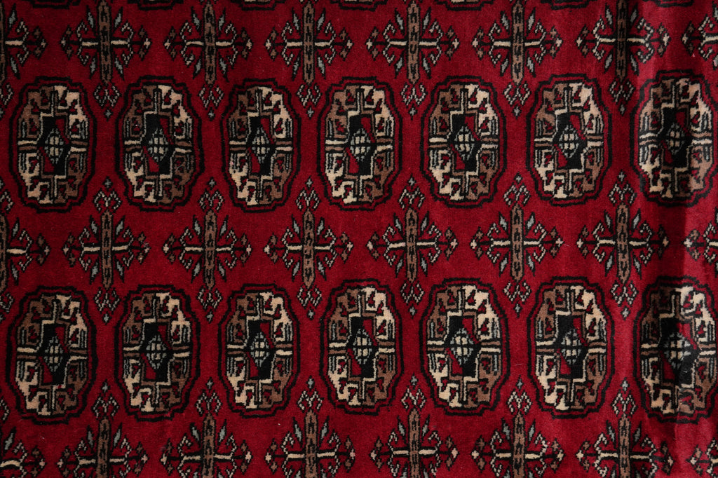 A close-up of a red patterned textile or rug with repeating ornate medallion motifs in beige, black, and dark red.
