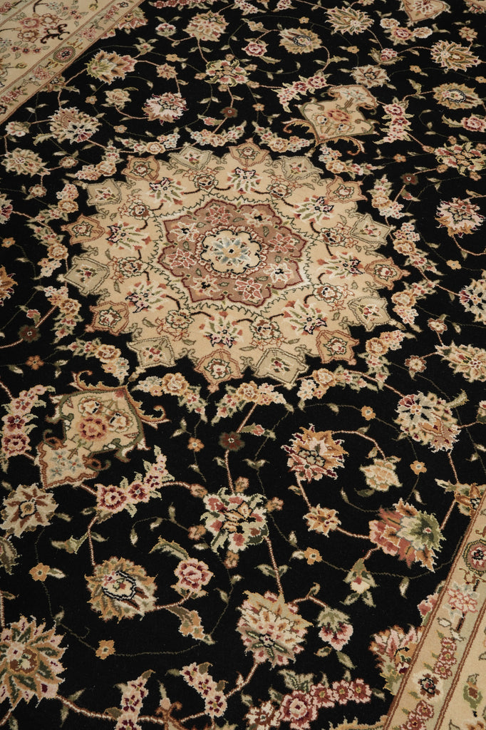 A close-up of an ornate traditional rug with a black field, beige central medallion, and floral motifs in beige, pink, and muted green.