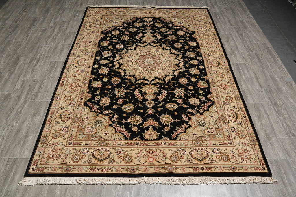 A rectangular traditional area rug with a black central field, beige and cream floral motifs, and a patterned border, shown on a gray wood-look floor.