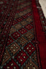 Load image into Gallery viewer, A close-up of a patterned rug with geometric diamond motifs in deep red, brown, black, and cream, showing the woven texture and fringe along the bottom edge.