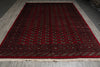 Load image into Gallery viewer, A large traditional oriental area rug with a deep red field, intricate dark blue and beige geometric patterns, and a fringed edge, displayed on a gray wood-plank floor.