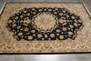 Load image into Gallery viewer, A large traditional oriental area rug with an intricate floral pattern, featuring a black central field, beige borders, and multicolored floral details, laid out on a gray tiled floor.