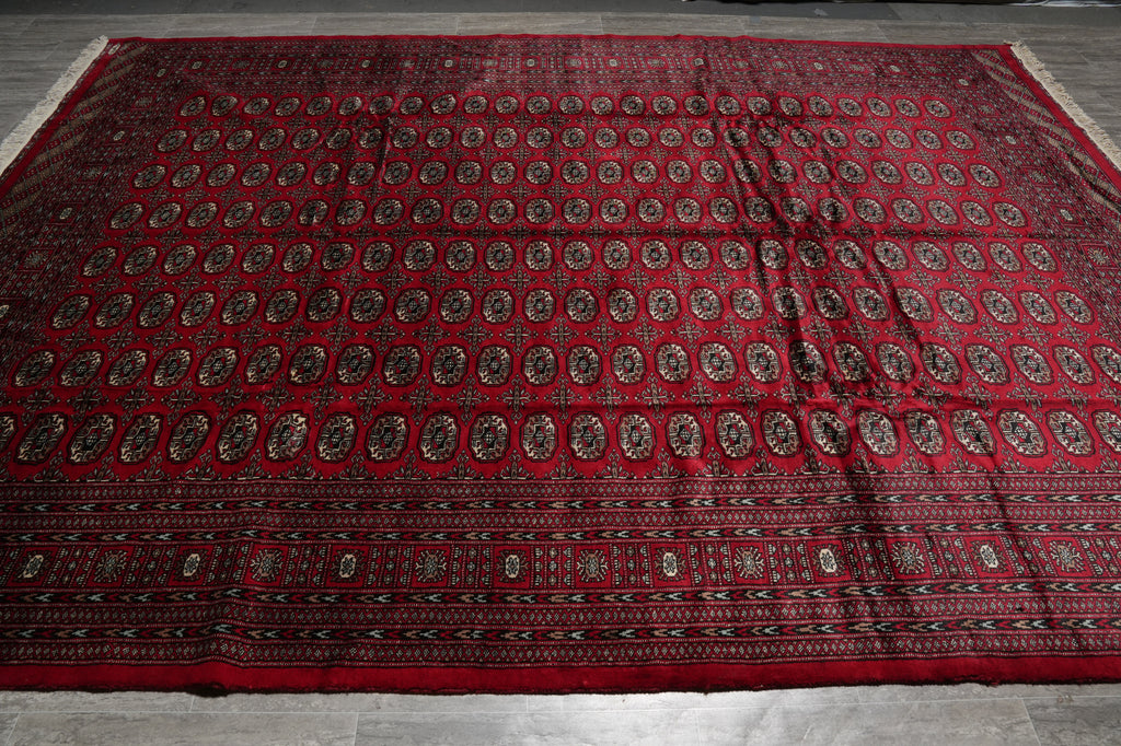 A large red Persian-style area rug with intricate black, brown, and beige geometric and floral patterns, laid flat on a gray tiled floor.