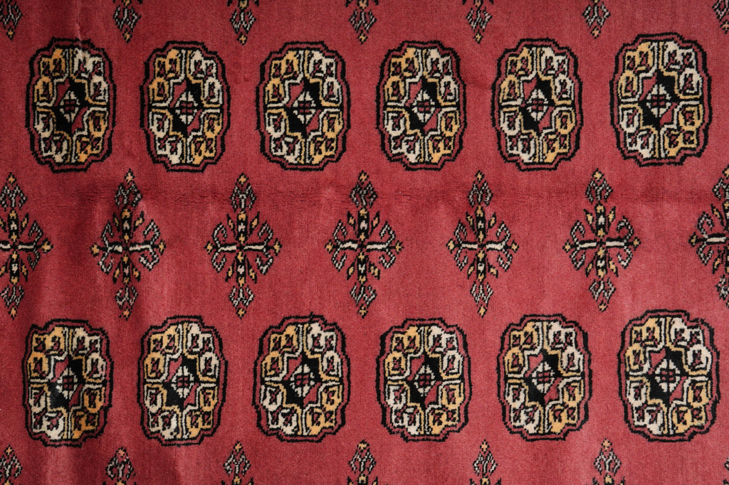 A close-up of a red patterned rug or textile featuring repeating geometric medallion motifs in black, beige, and muted gold tones.