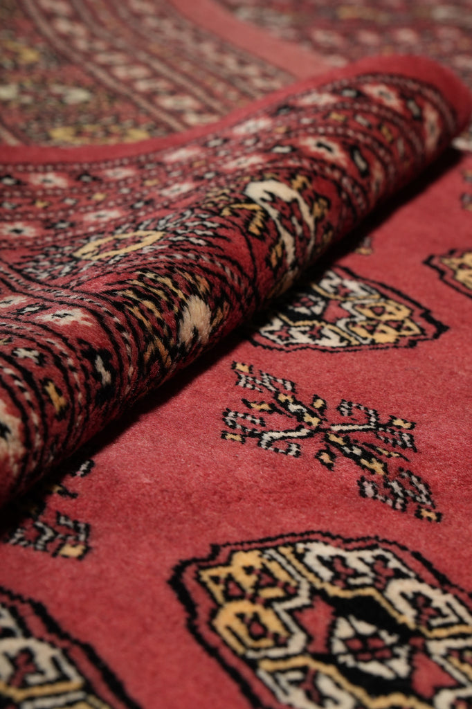 A close-up of a folded red patterned rug showing detailed woven motifs in cream, black, and yellow.