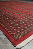 Load image into Gallery viewer, A red Persian-style area rug with intricate geometric and floral motifs, featuring a white fringed edge, shown laid out on a gray concrete floor.