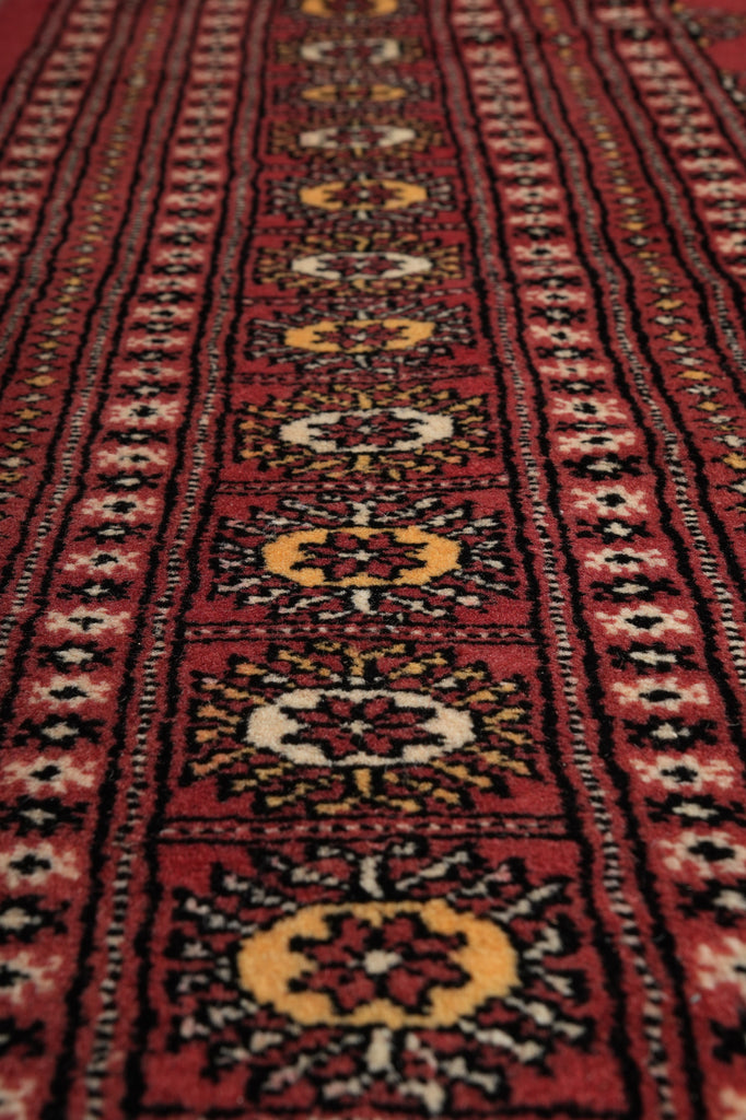 A close-up view of a traditional patterned rug with a deep red field, black borders, and repeating medallion motifs in yellow, cream, and brown.
