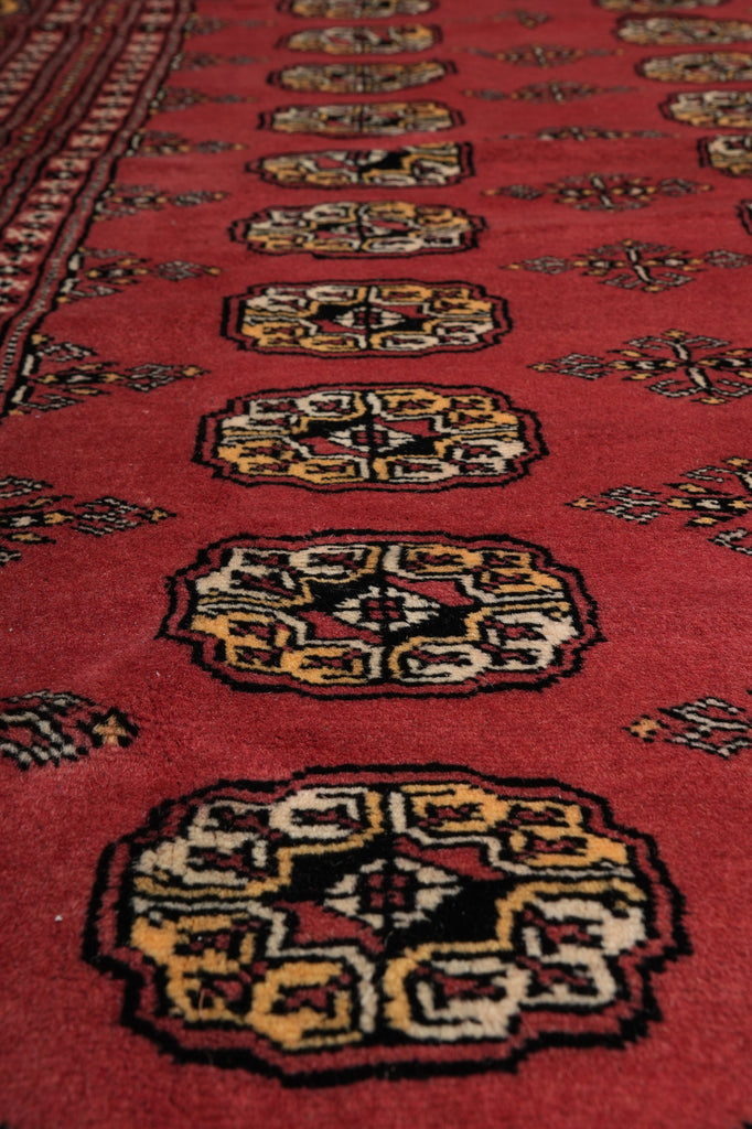 A close-up view of a red patterned rug with ornate medallion motifs in cream, black, and gold tones.