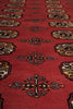 Load image into Gallery viewer, A close-up view of a red patterned rug with repeating geometric and floral motifs in black, beige, and muted yellow.