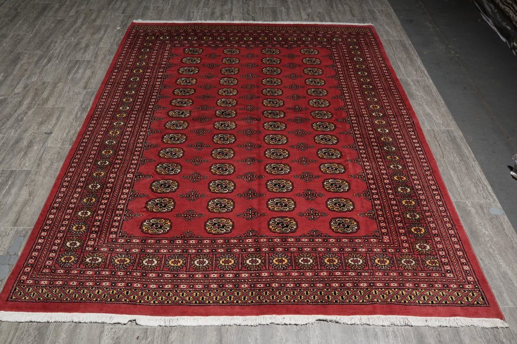 A rectangular red Persian-style area rug with intricate black, gold, and beige patterns, laid out on a gray wood-plank floor.