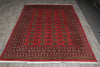 Load image into Gallery viewer, A rectangular red Persian-style area rug with intricate black, gold, and beige patterns, laid out on a gray wood-plank floor.