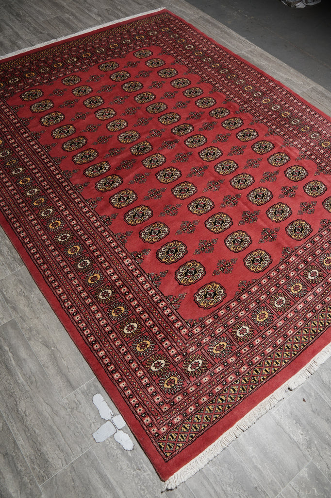 A red Persian-style area rug with intricate circular medallion patterns and detailed borders, shown laid out on a gray tiled floor.