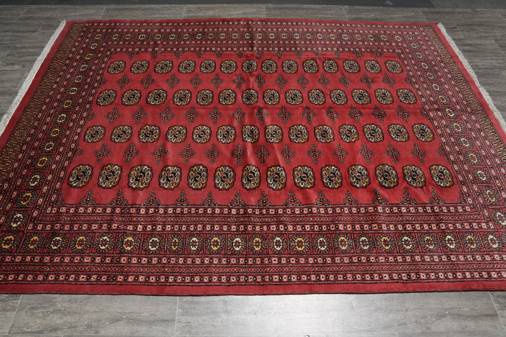 A large red Persian-style area rug with intricate black, gold, and beige geometric patterns, laid out on a gray tiled floor.
