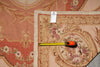 Load image into Gallery viewer, A close-up of a vintage-style floral tapestry rug with a dusty rose and beige background, featuring a yellow tape measure and a small white tag placed on it for scale.