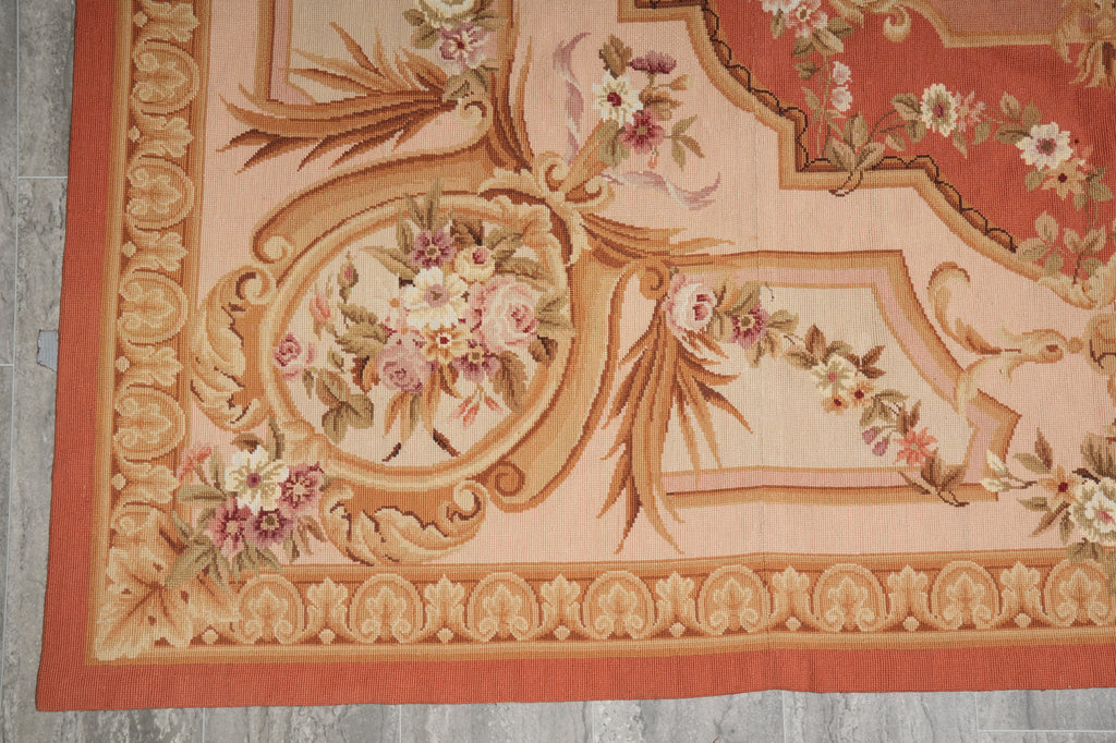 A close-up of a traditional patterned rug featuring a warm peach and rust orange background with ornate floral bouquets and scrollwork in beige, gold, and muted pink.
