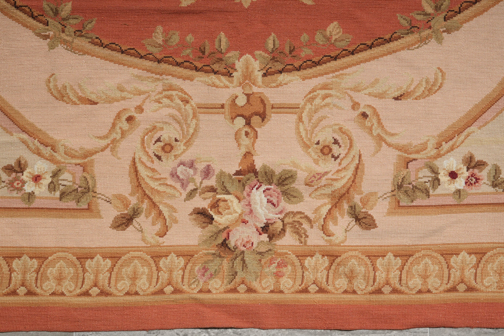 A close-up of a decorative woven textile or rug pattern with floral motifs, scrolling acanthus leaves, and a warm peach and beige palette.