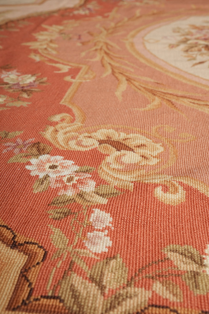 Close-up of a woven textile with a floral and scroll pattern in terracotta, peach, beige, and cream tones.