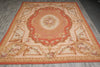 Load image into Gallery viewer, A large rectangular area rug with a classic French Empire or Louis XV style medallion pattern, laid out on a gray wood-plank floor. The rug features a warm peach and orange border, a central cream medallion with floral details, and ornate scrollwork in beige and gold tones.