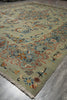 Load image into Gallery viewer, A traditional oriental area rug with a sage green base and intricate floral patterns in blue, orange, beige, and white, shown laid out on a gray concrete floor.
