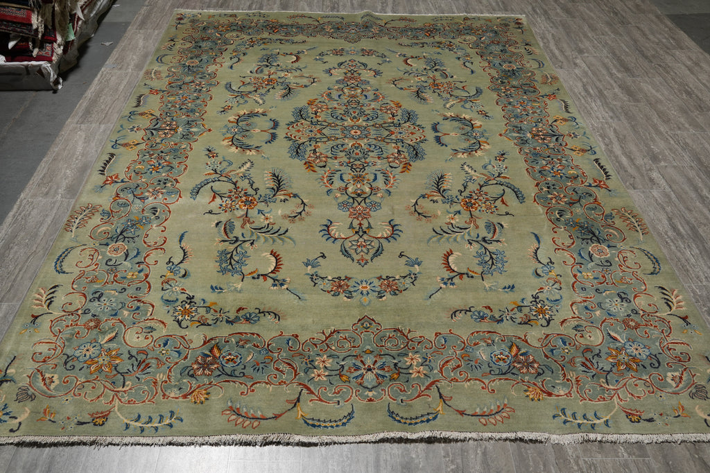 A large traditional oriental area rug with a central medallion and ornate floral border, shown laid out on a gray wood floor.
