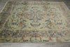 Load image into Gallery viewer, An ornate traditional area rug with a central medallion and floral motifs, featuring a muted sage green background with blue, rust orange, and beige details, laid out on a gray wood floor.