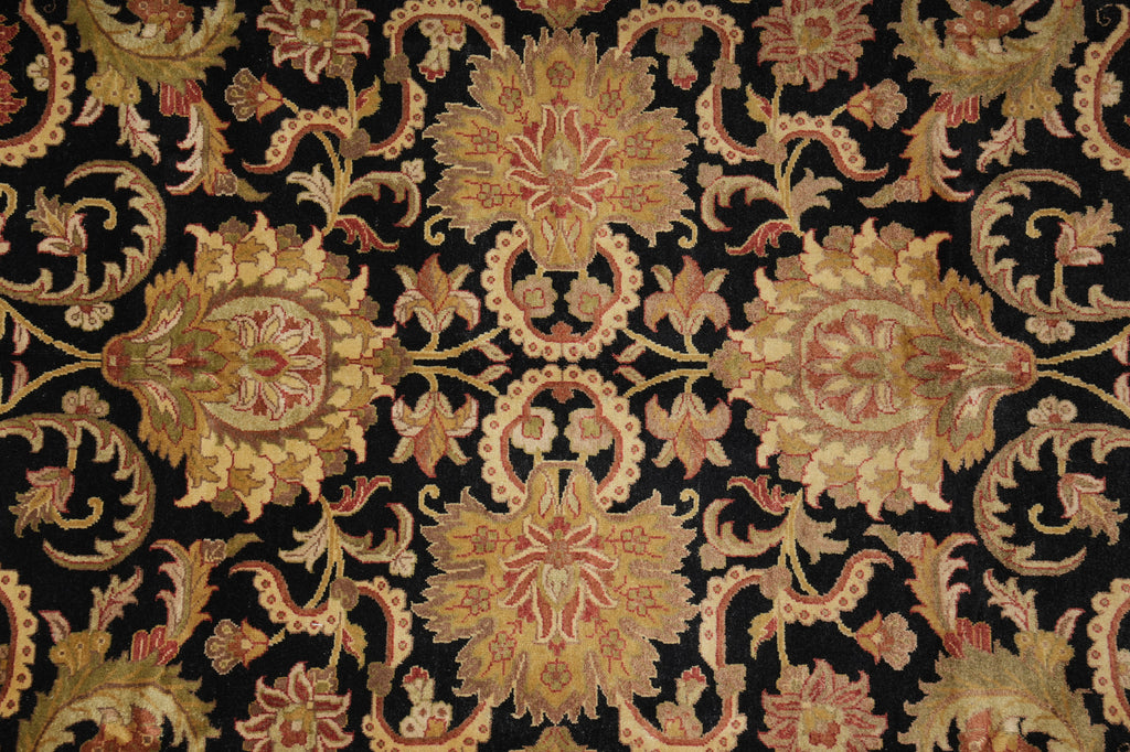 A close-up of an ornate damask-style textile or rug pattern with large floral motifs on a black background, featuring gold, beige, and muted red tones.