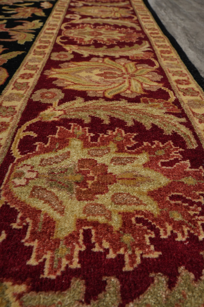 A close-up view of a traditional patterned area rug with a deep red field, beige and gold floral motifs, and a dark border.