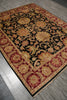 Load image into Gallery viewer, An ornate rectangular area rug with a traditional floral pattern, shown laid out on a gray wood floor. The rug features a black center field surrounded by red and gold borders, with detailed floral motifs.