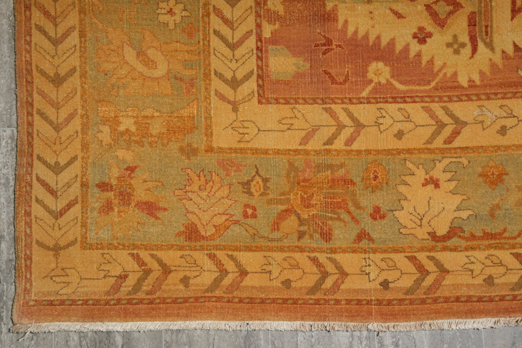 Close-up of an antique-style patterned rug corner showing a warm orange and beige floral design on a muted sage green field.