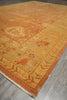 Load image into Gallery viewer, A square area rug with a traditional floral pattern in warm shades of ochre, mustard, and terracotta, laid out on a gray wood floor.
