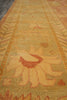 Load image into Gallery viewer, A close-up view of a patterned area rug with a warm mustard yellow and beige base, featuring a central floral motif in rust red and orange, bordered by geometric patterns.