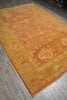 Load image into Gallery viewer, A rectangular area rug with a warm orange and beige central field and a contrasting olive green border, laid out on a gray wood floor.