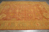 Load image into Gallery viewer, An antique-style oriental area rug with a faded orange and ochre center field, decorated with traditional motifs and a detailed patterned border, laid out on a dark gray tiled floor.