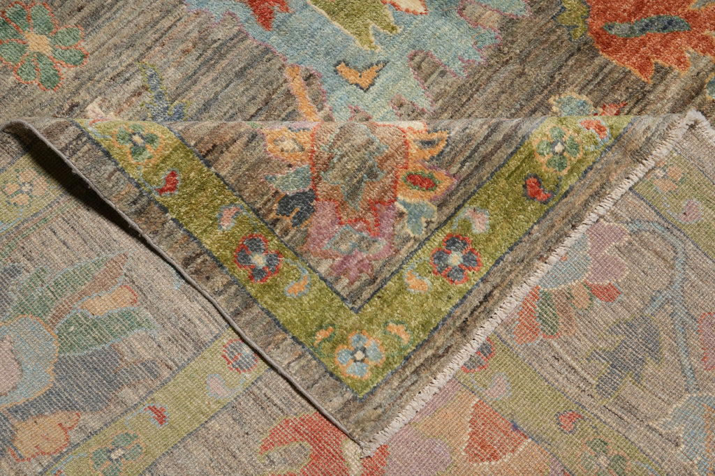 A close-up of an ornate area rug corner showing a folded V-shaped border with a muted green floral pattern over a distressed gray and beige field.