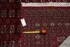 Load image into Gallery viewer, A traditional patterned area rug in deep red with geometric and floral motifs, shown with a yellow tape measure and a white product tag on a dark surface.
