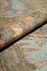 Load image into Gallery viewer, A close-up of a multicolored area rug with a rolled section showing its textured pile and vintage-style abstract pattern.