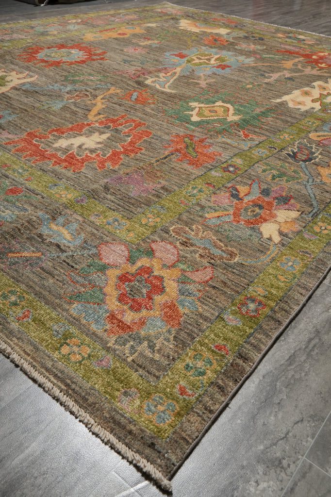 A rectangular area rug with a distressed, vintage-style floral pattern in muted earthy tones, shown laid out on a gray tiled floor.