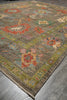 Load image into Gallery viewer, A rectangular area rug with a distressed, vintage-style floral pattern in muted earthy tones, shown laid out on a gray tiled floor.