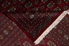 Load image into Gallery viewer, A close-up of a traditional patterned rug with a deep red background, intricate geometric and floral motifs in black, beige, and blue, and a white fringed edge.