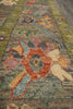 Load image into Gallery viewer, A close-up view of a traditional area rug with a floral pattern in muted earthy tones, featuring a central rust-orange flower, beige cherub motifs, and green borders.