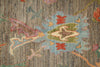 Load image into Gallery viewer, Close-up of a textured area rug featuring a central floral or medallion motif in muted blue, olive green, coral red, cream, and pink over a vertically striped taupe-brown background.