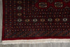 Load image into Gallery viewer, A close-up of a traditional patterned rug corner, showing a deep red field with intricate geometric and floral motifs in black, beige, and orange, finished with a cream-colored fringe.