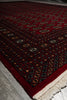 Load image into Gallery viewer, A close-up of a traditional patterned rug with a deep red field, cream fringe, and dark navy and beige geometric motifs.